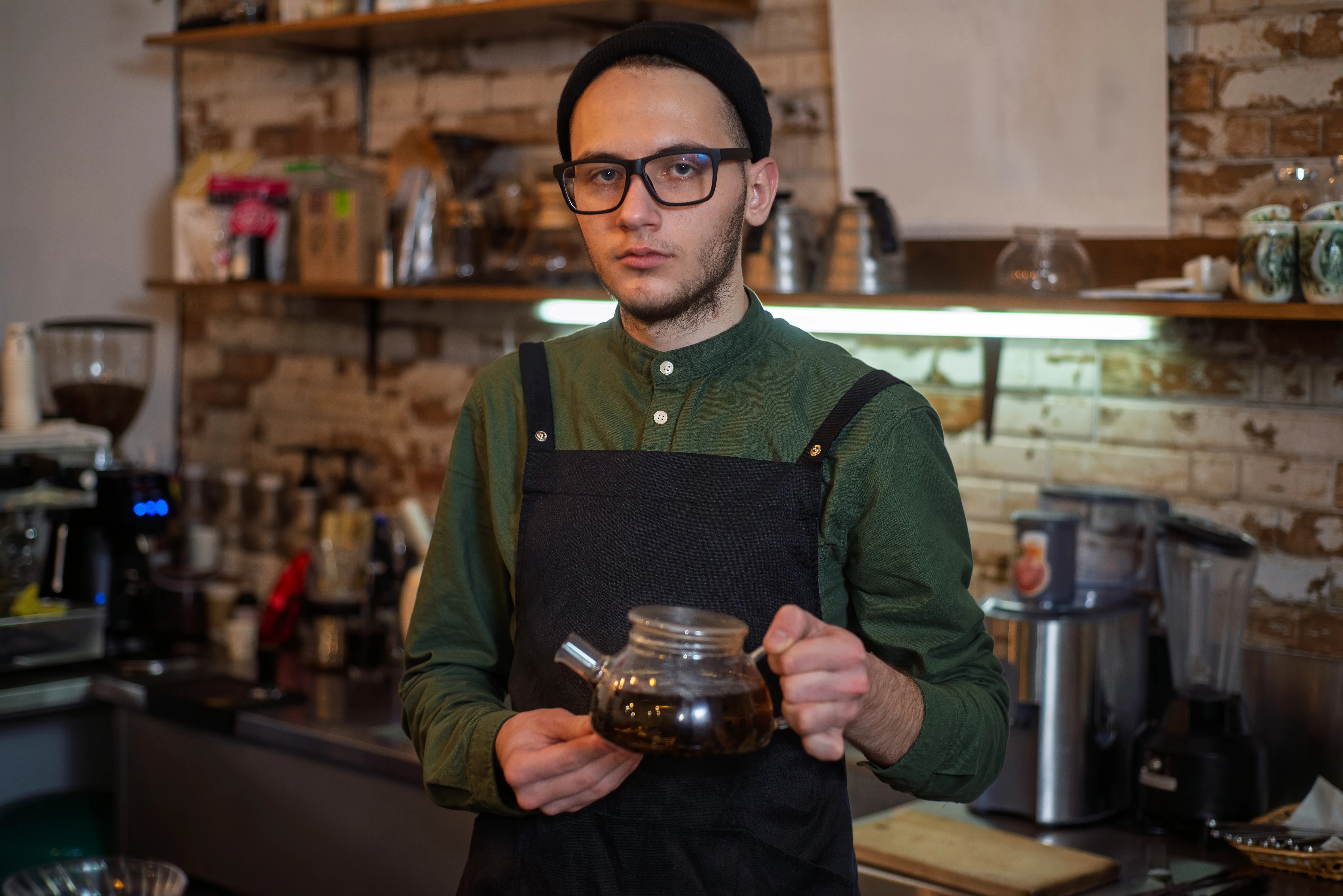 A roaster in an apron behind the counter, holding a glass brewing pot