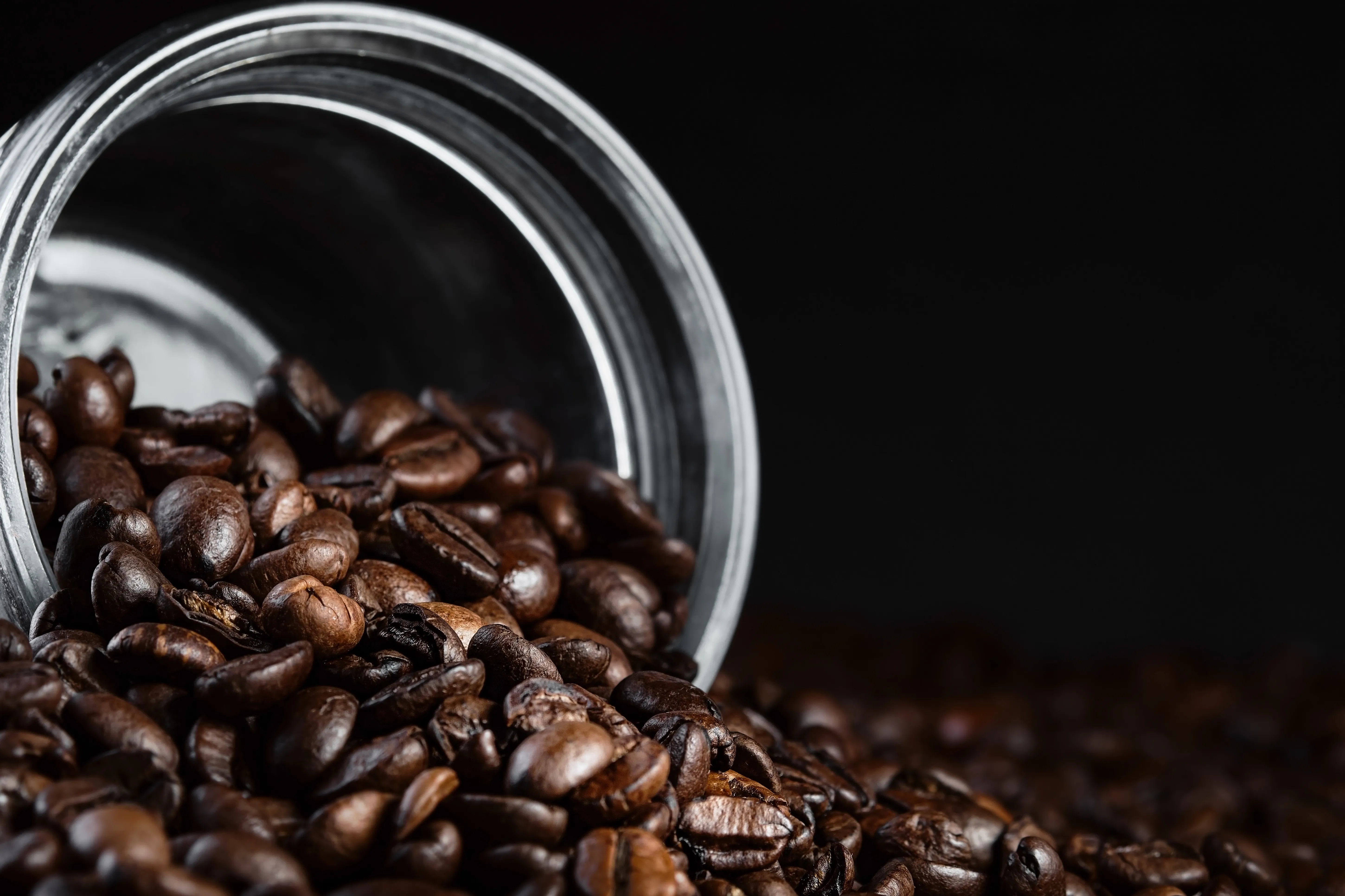 Roasted coffee beans spilling from a tipped glass jar